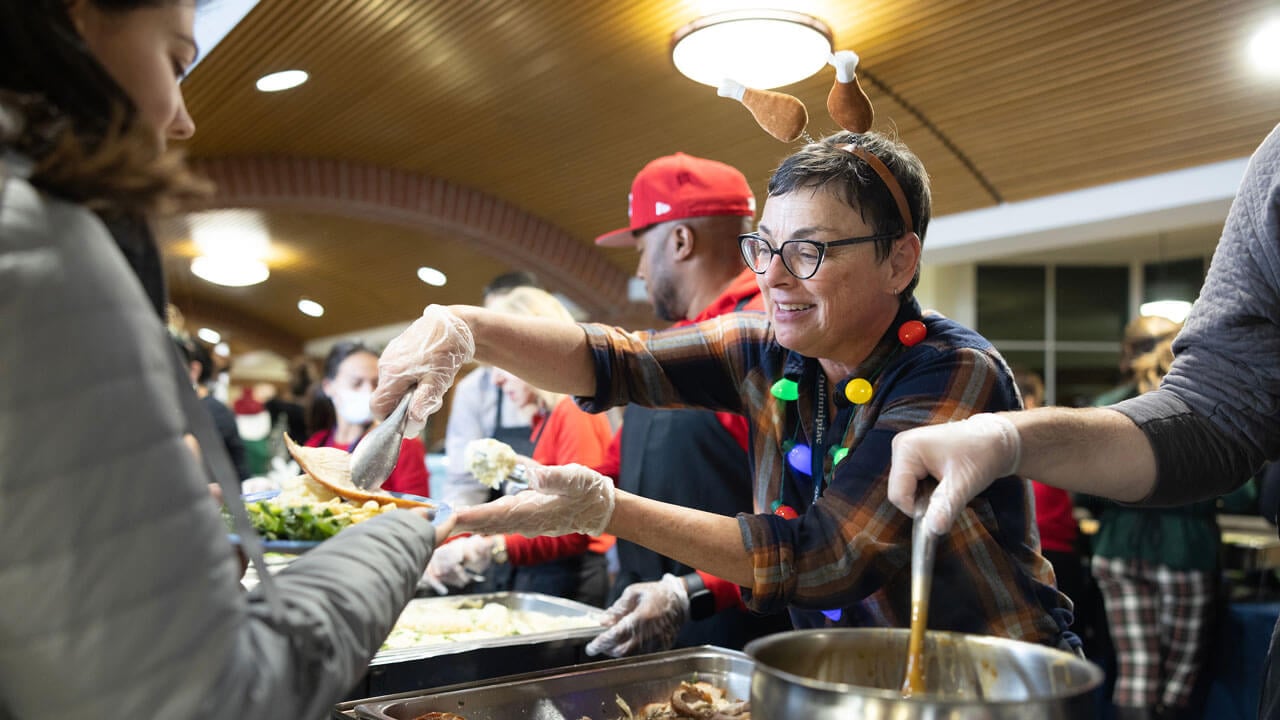 Faculty member serves food at the annual undergraduate holiday dinner.
