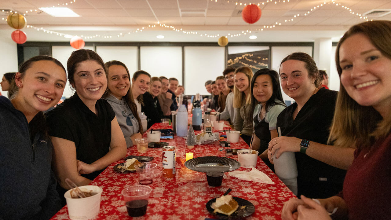 Graduate students sit together at table with their food and smiles on their faces