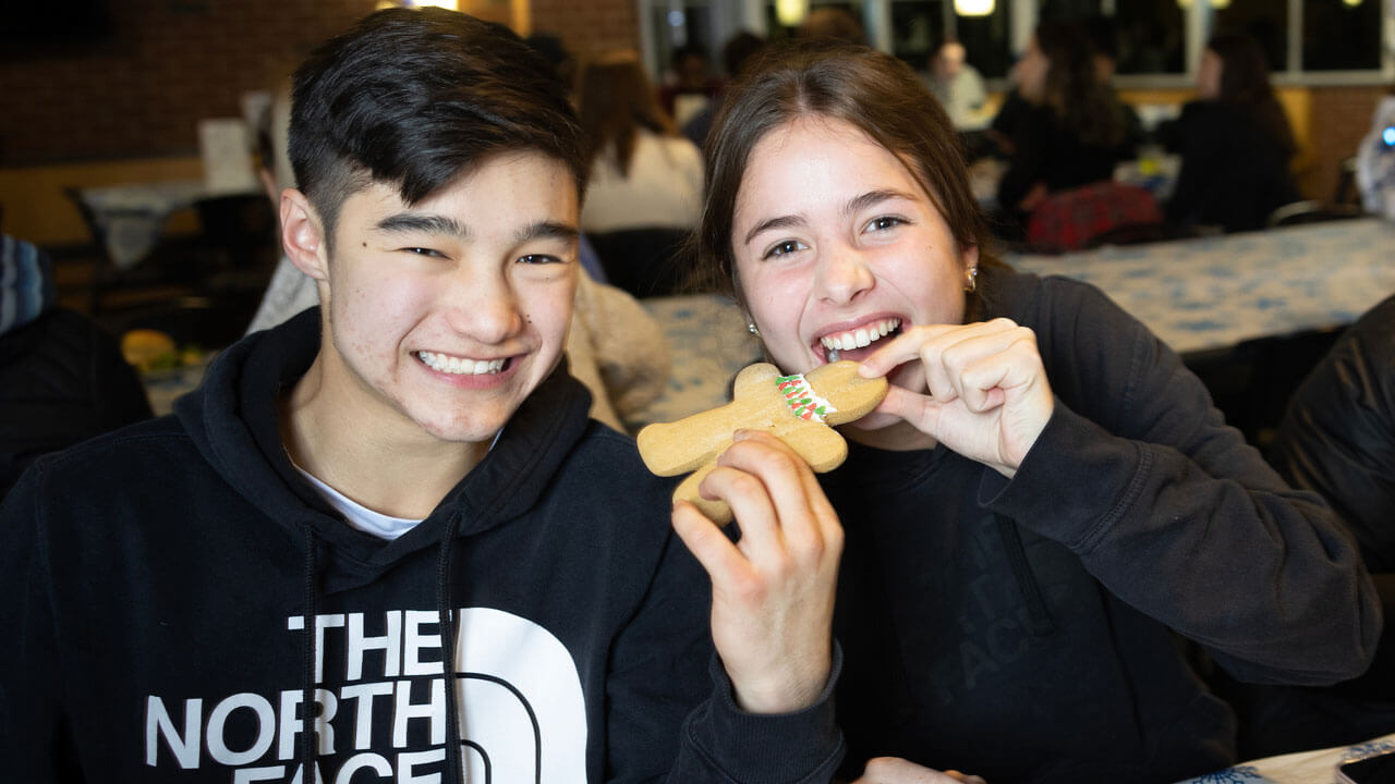 Two students eat a ginger bread man at the undergraduate holiday dinner.