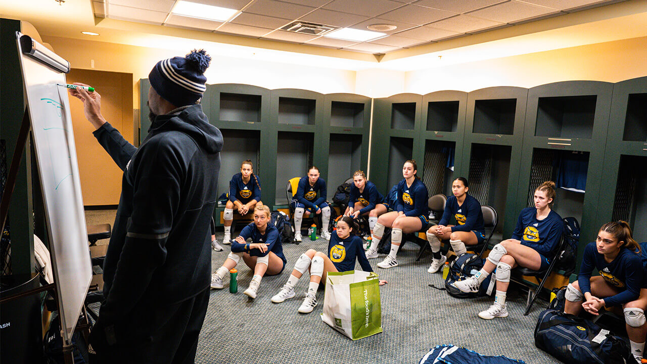 The team listening to their coach in the locker room prior to the game.