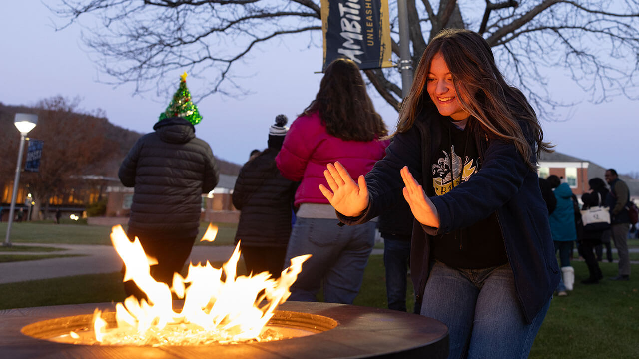 Student warming her hands by the fire pit on the quad