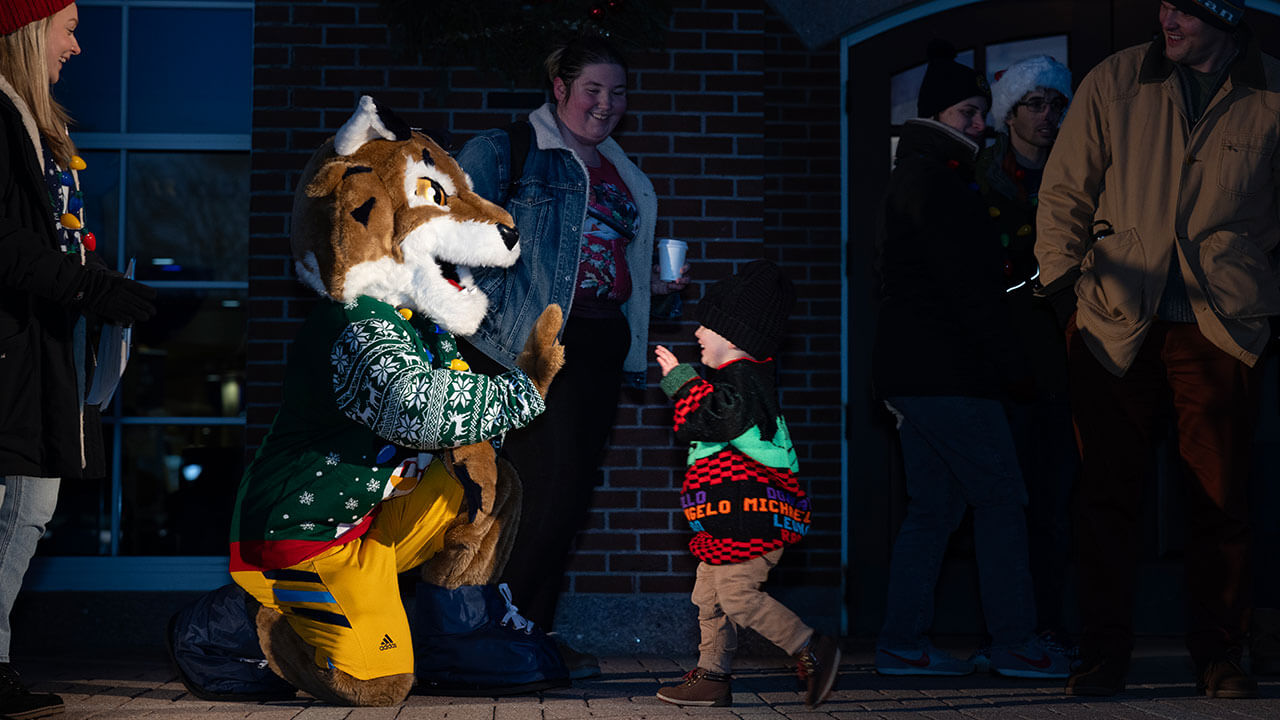 Boomer the Bobcat high-fiving a child in holiday spirit wear