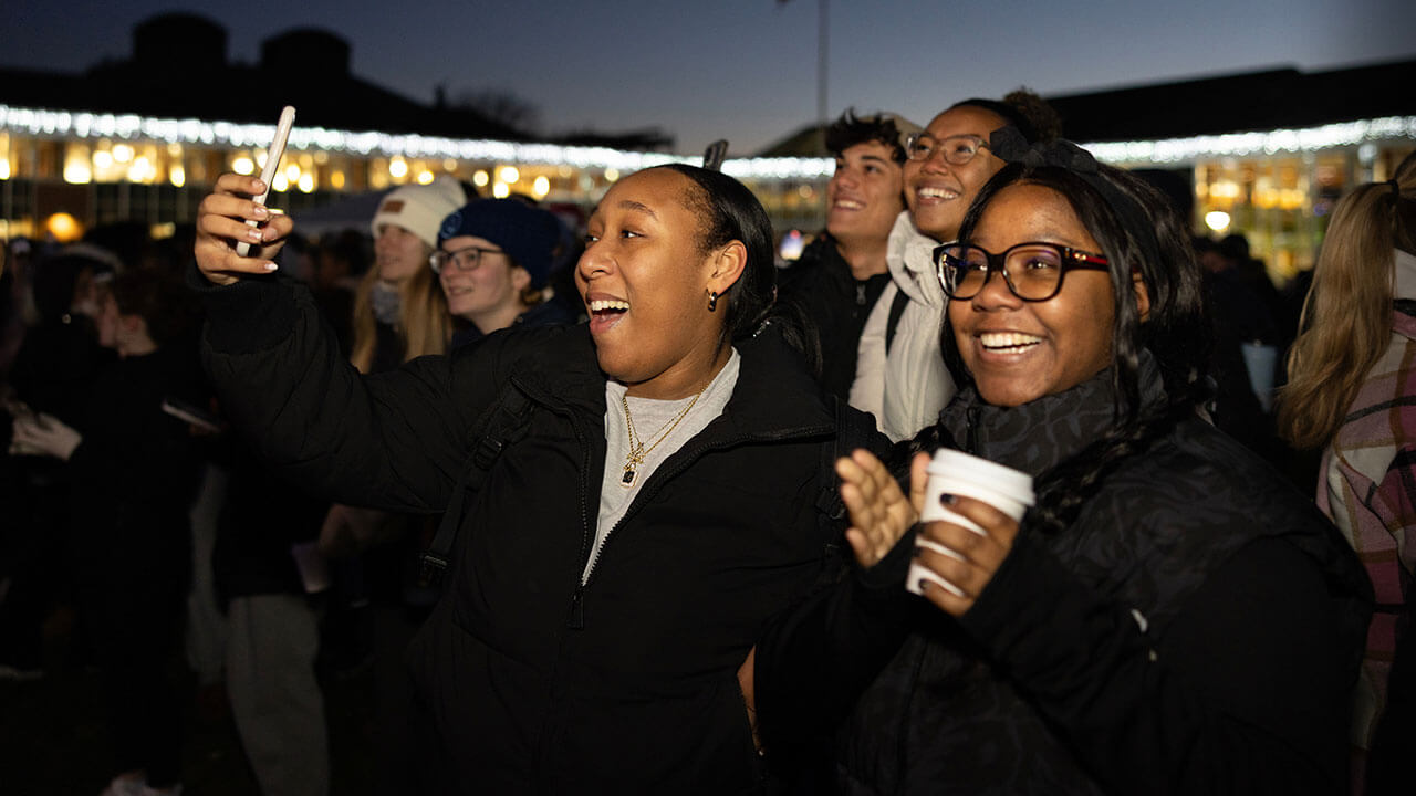 Students take pictures and smile during the quad lighting
