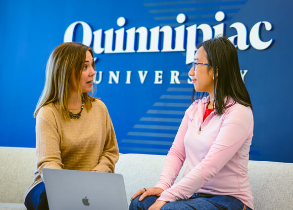 Two people sit and talk with a laptop in the Quinnipiac admissions and financial aid visitors center