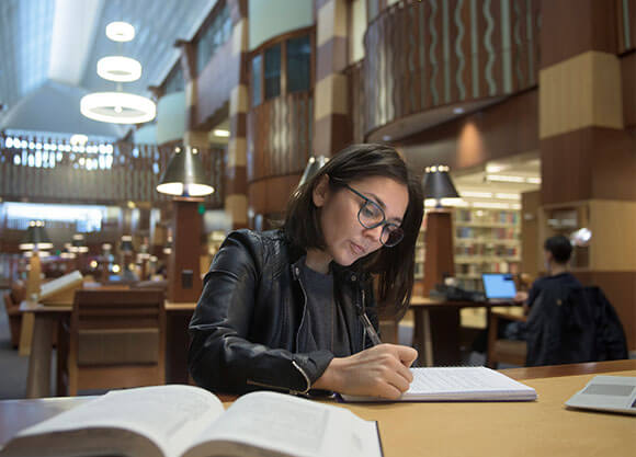 woman writing in notebook inside of a library