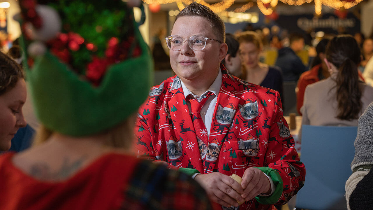 Attendee smiles and talks to others while wearing a holiday, cat-themed suit