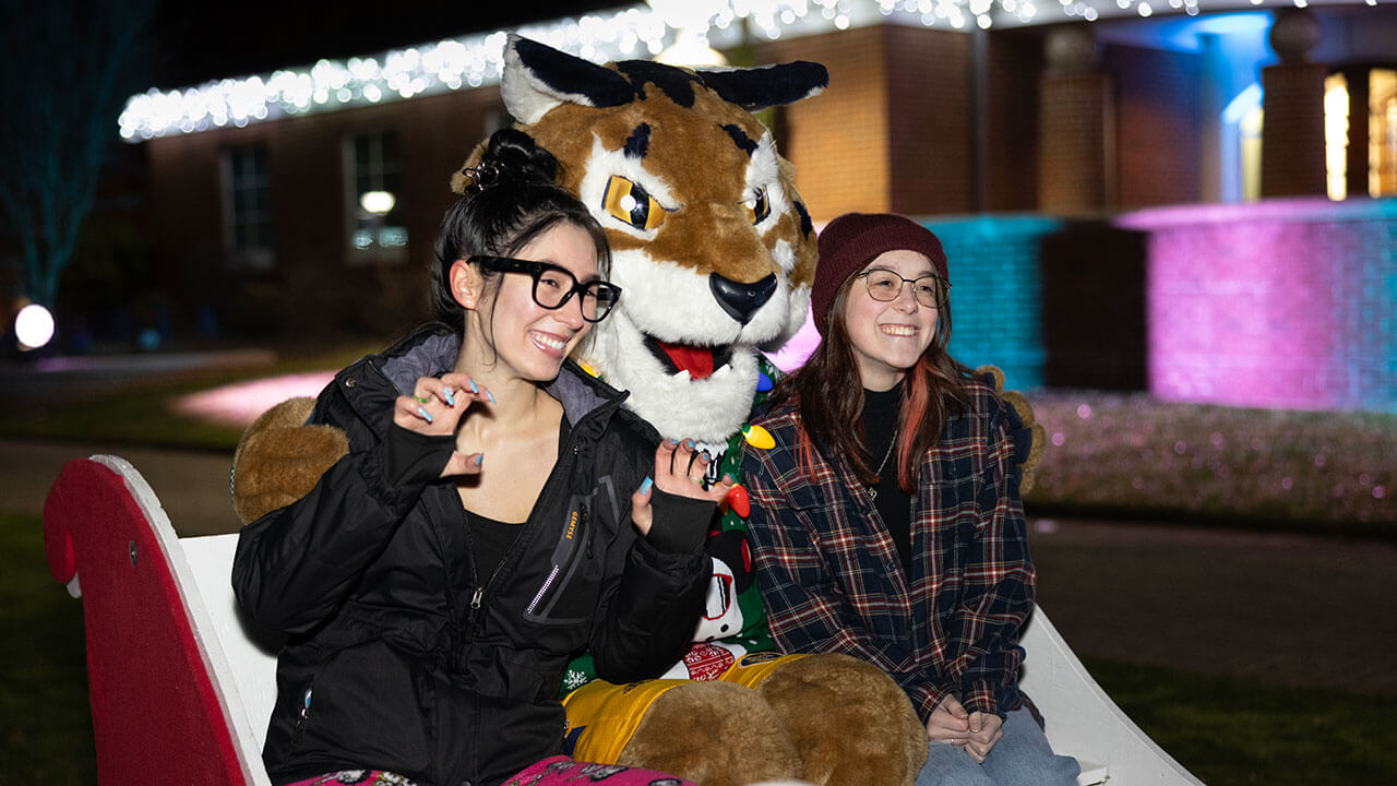 Girls smiling with Boomer the Bobcat on a sleigh