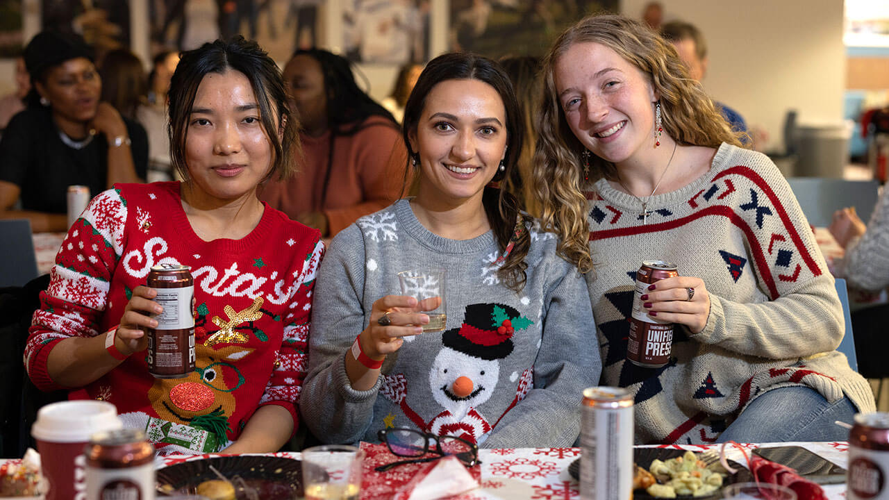 Three women raise their glasses at the Graduate Holiday Dinner
