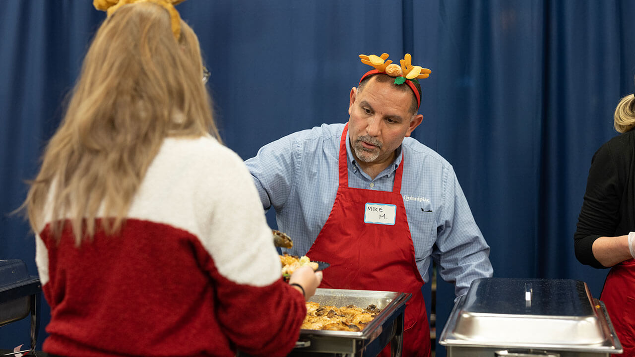 A volunteer serves graduate students dinner during a holiday celebration