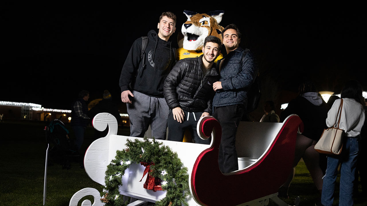 Students smile with Boomer in a sleigh during the Quad lighting