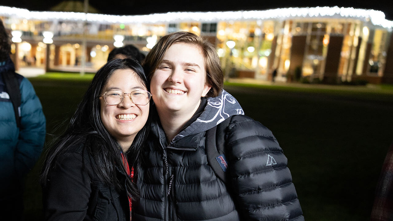 Students smile in front of the holiday lights on the Quad