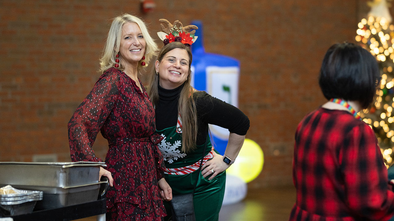 Two Quinnipiac faculty members wearing holiday sweaters smile.