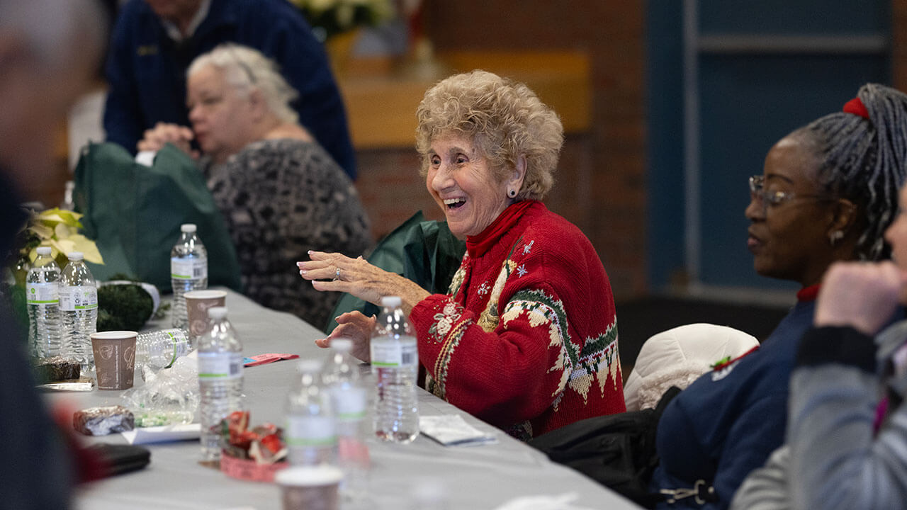 A senior citizen sits at a dinner table and laughs with peers.