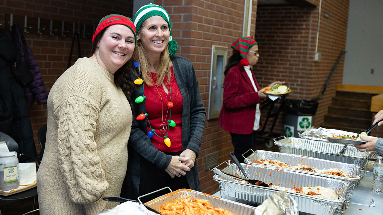 Volunteers serve food while wearing Christmas sweaters.