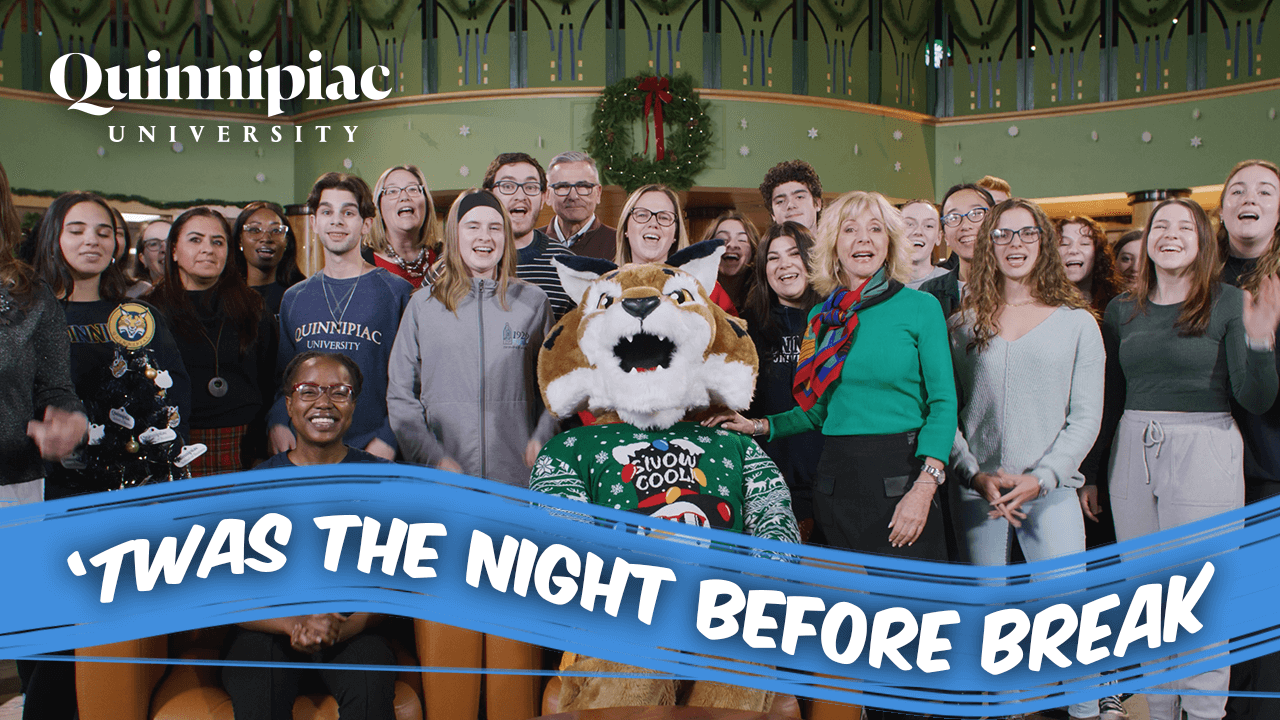 A group of Quinnipiac student smile with Boomer and President Olian with words overlaying "twas the night before break"
