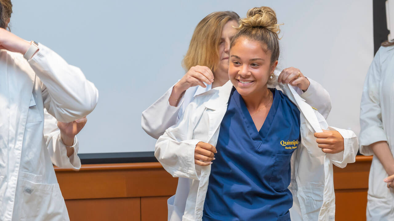 A nursing student smiles as they put on their white coat.
