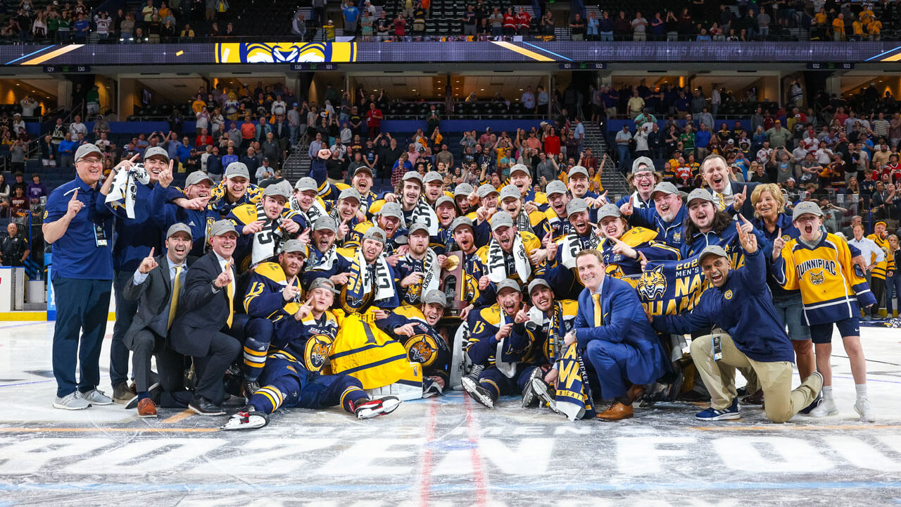 The entire men's ice hockey team and coaches smile wide on the ice after the national championship win.