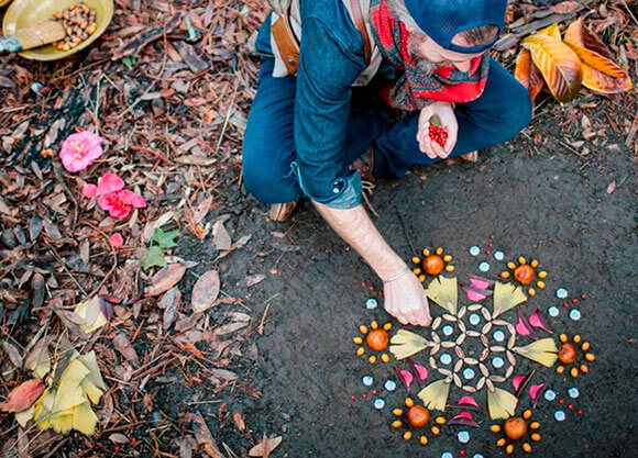 A man creates a piece of art outside on the ground using things found in nature