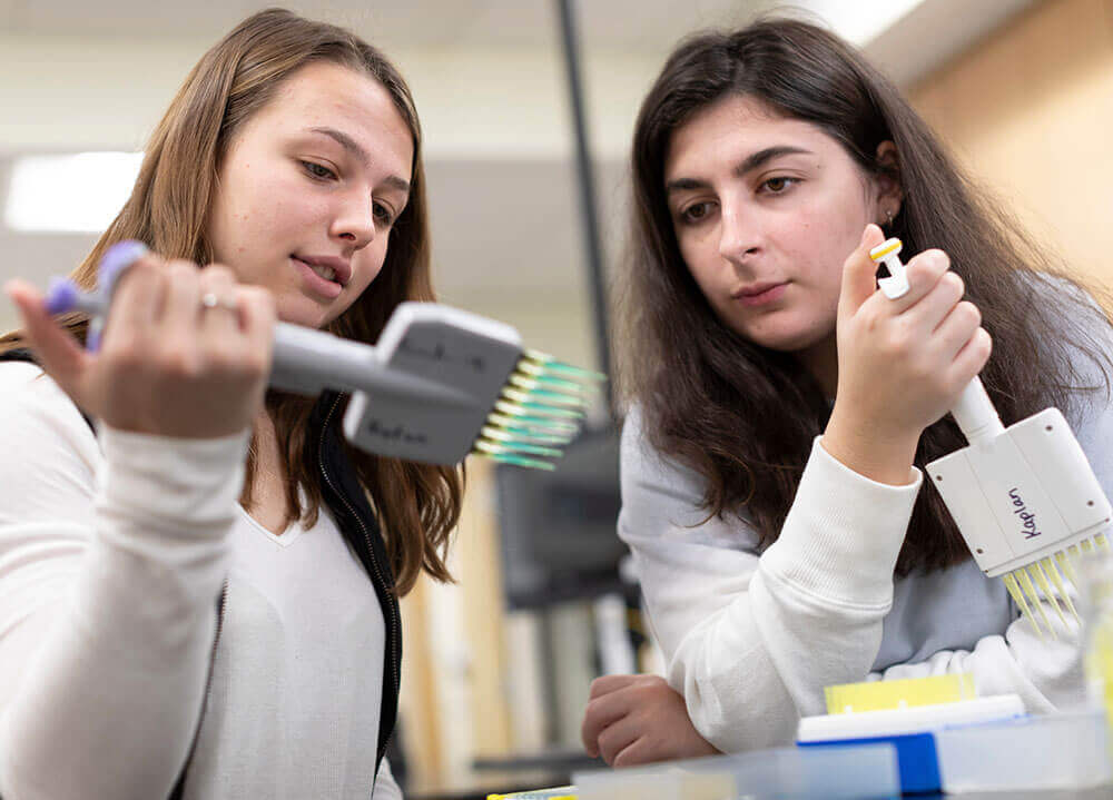Two biology students sit side-by-side in a lab classroom conducting an experiment
