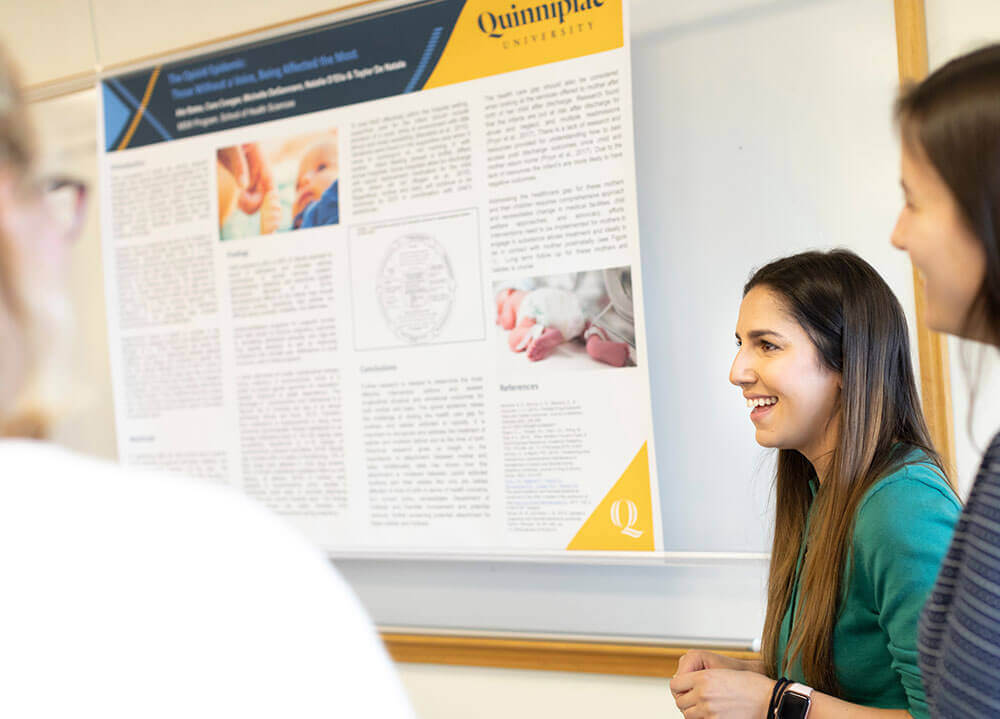 A social work student presents her work in poster format to two colleagues