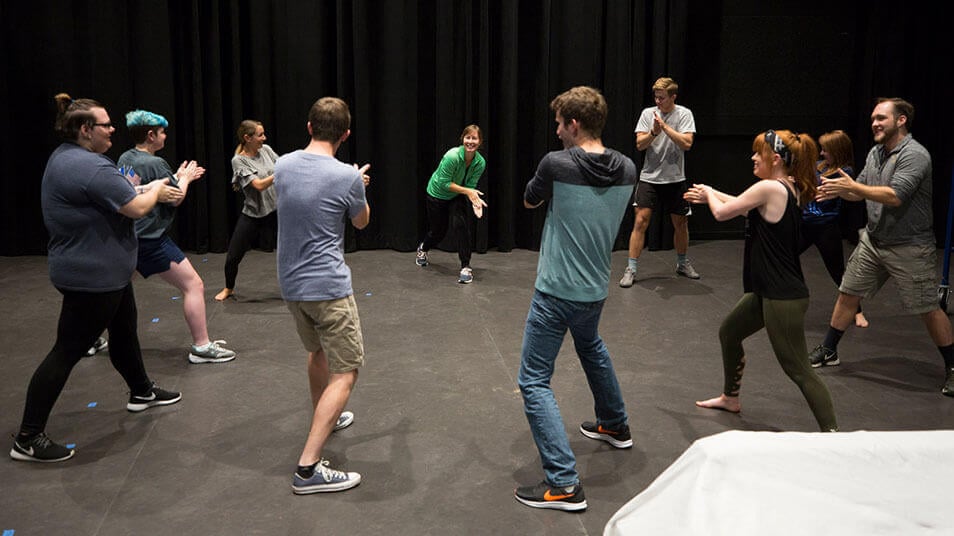 Theater students gather in a large circle during an audition exercise onstage