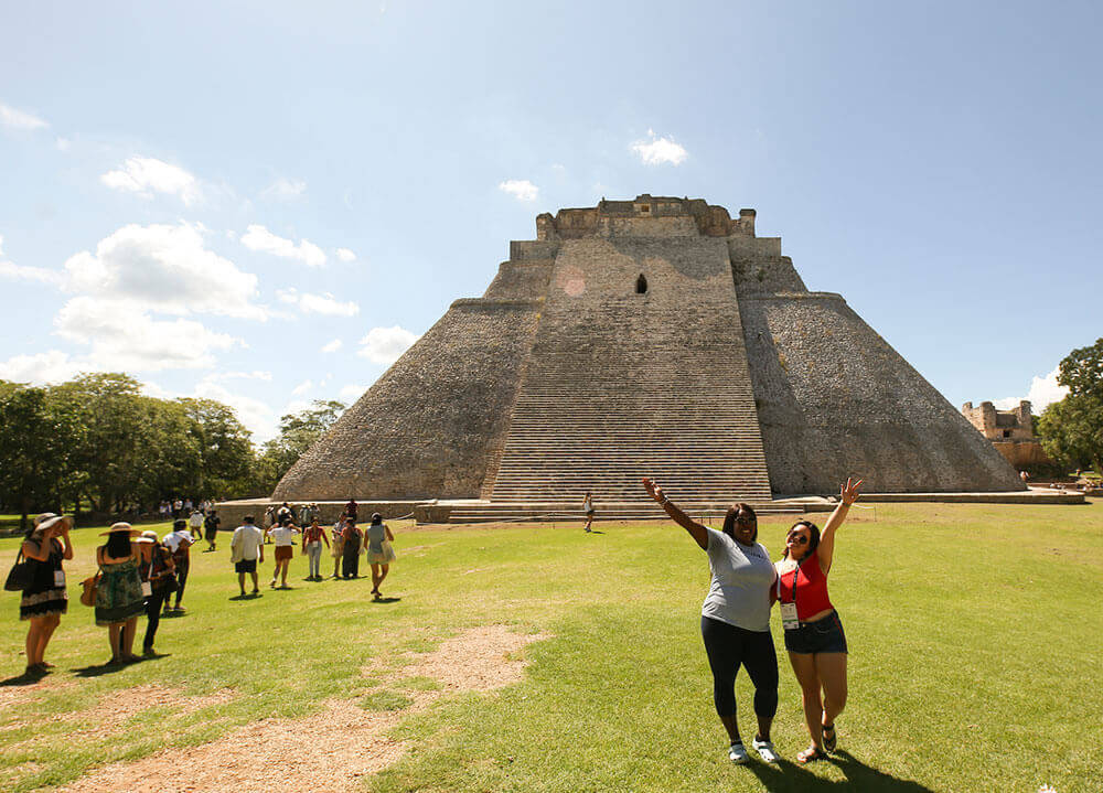 Two Quinnipiac students smile and pose in front of a large granite Mexican temple while abroad