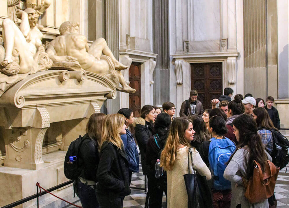 A group of students gather around ancient sculptures at a chapel in Florence, Italy