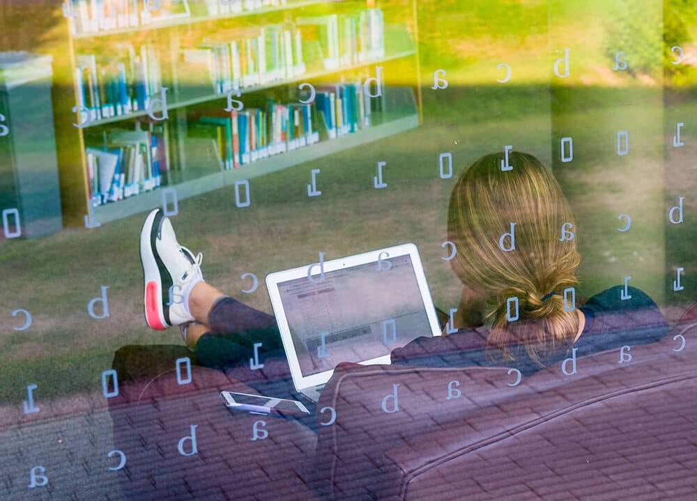 A student sits in a leather chair with her feet up and laptop on her lap in the Arnold Bernhard Library