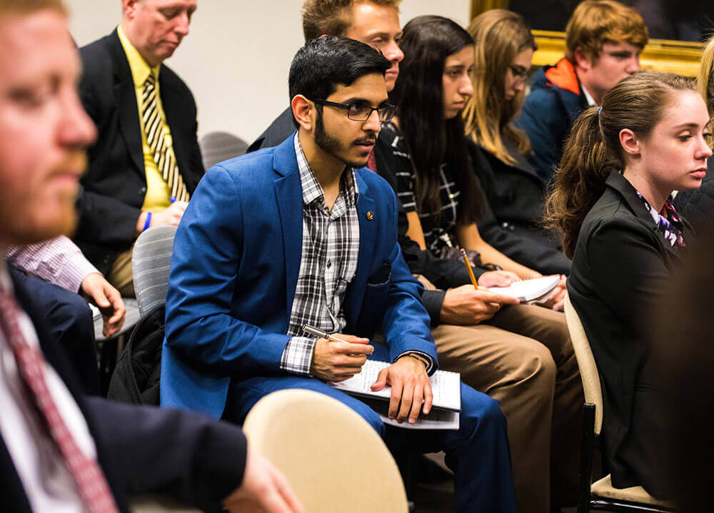 A political science student wearing a blue suit takes notes in the crowd at a lecture in Washington, D.C.