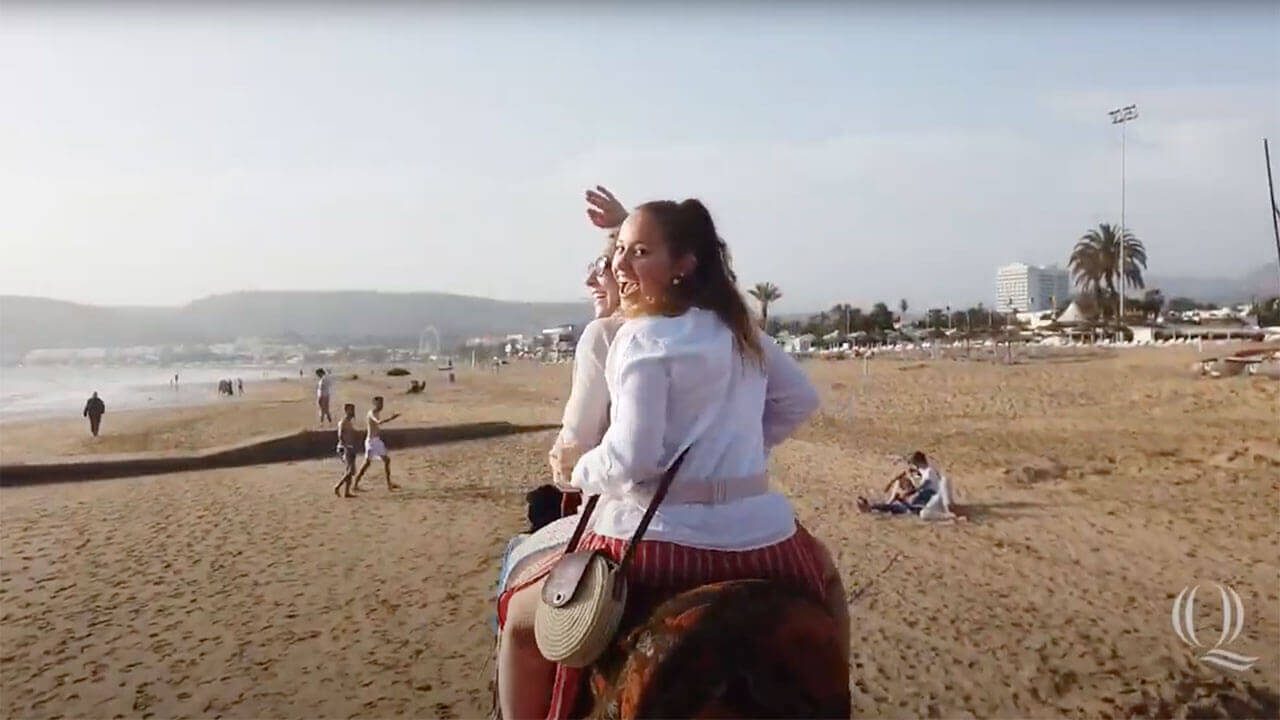 Two students ride on the back of a camel on a Moroccan beach, starts video