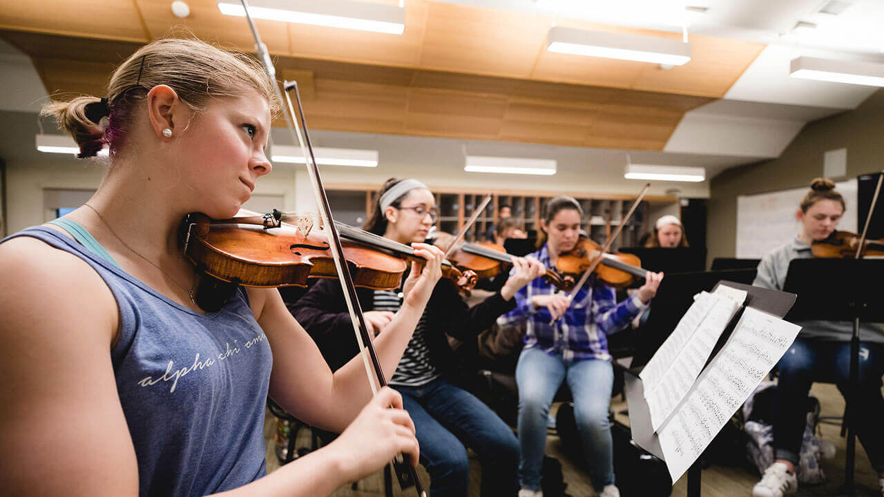 A group of music students play their violins in the Music Building