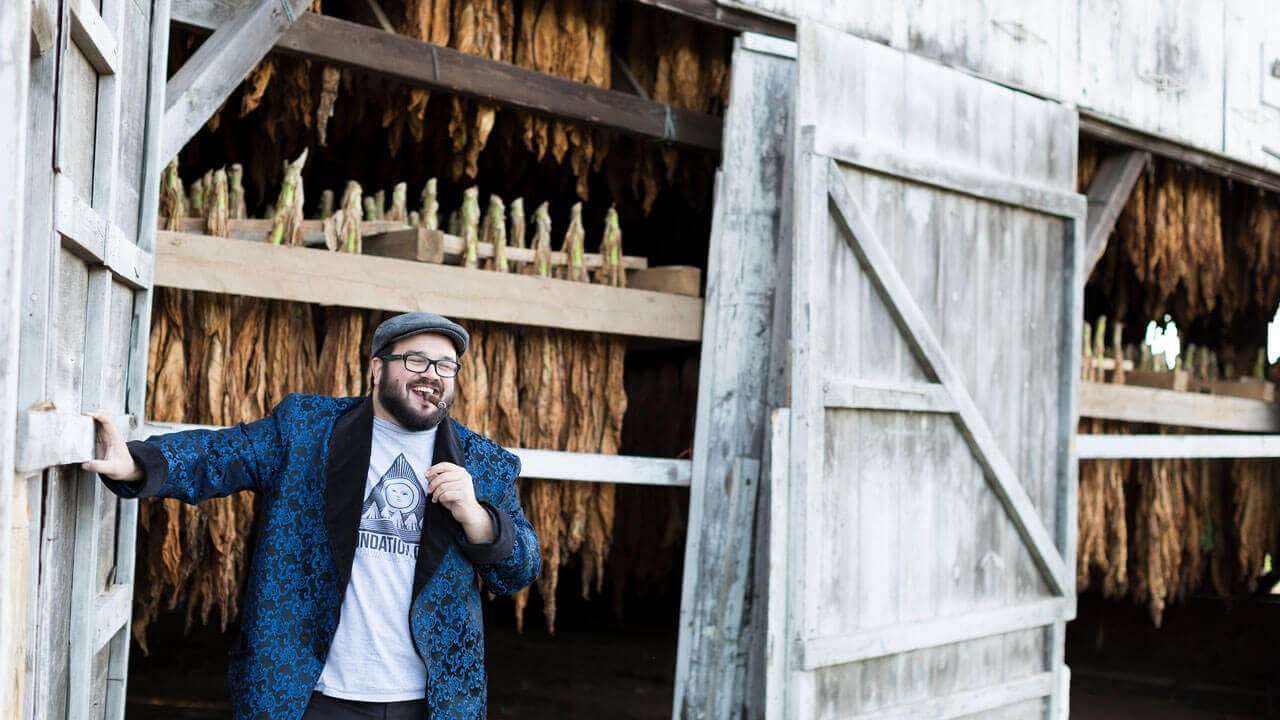 Nicholas Melillo smiles in front of his tobacco barns with a cigar in his mouth