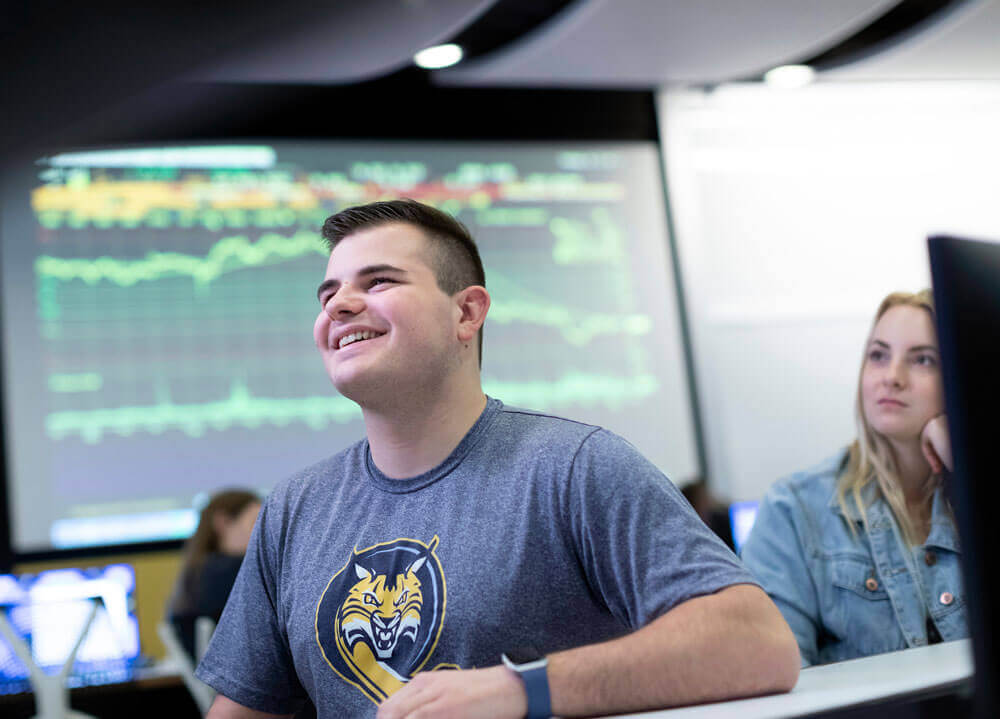 Students smiles during a lecture n the Lender School of Business Terry W. Goodwin ’67 Financial Technology Center at Quinnipiac’s Mount Carmel Campus