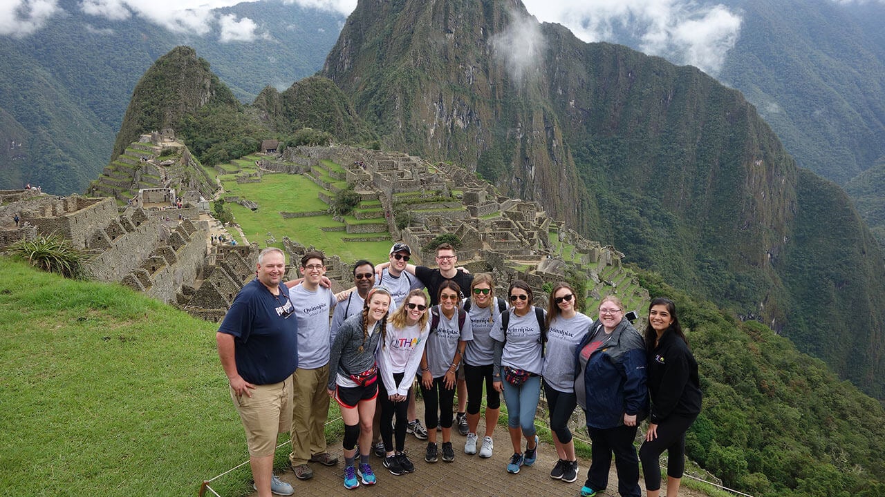 A group of students and professors pose in front of a mountain range