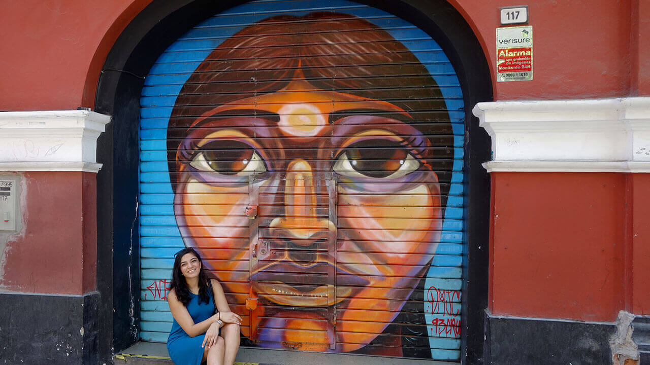 A student sits in front of a storefront with a large graffiti portrait