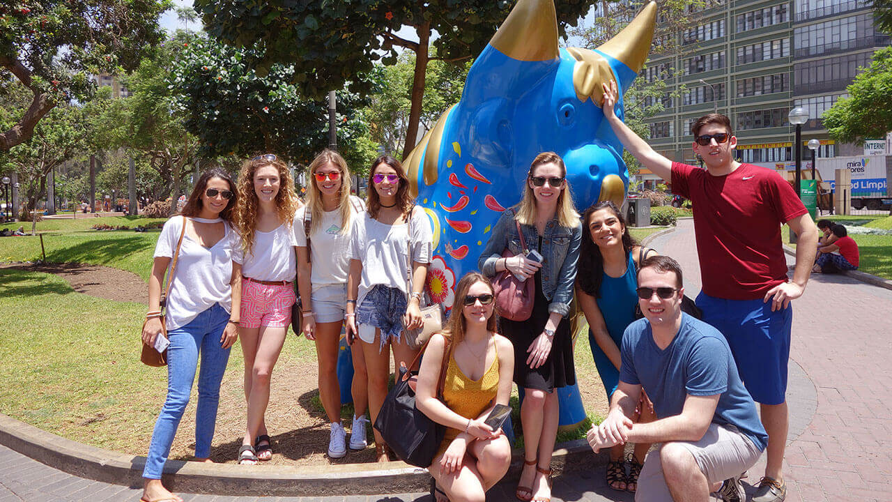 Students pose in front of a colorful blue bull statue in Peru