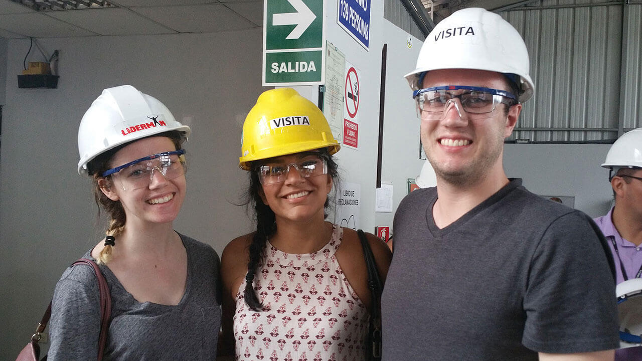Three students wear branded construction helmets onsite in Peru