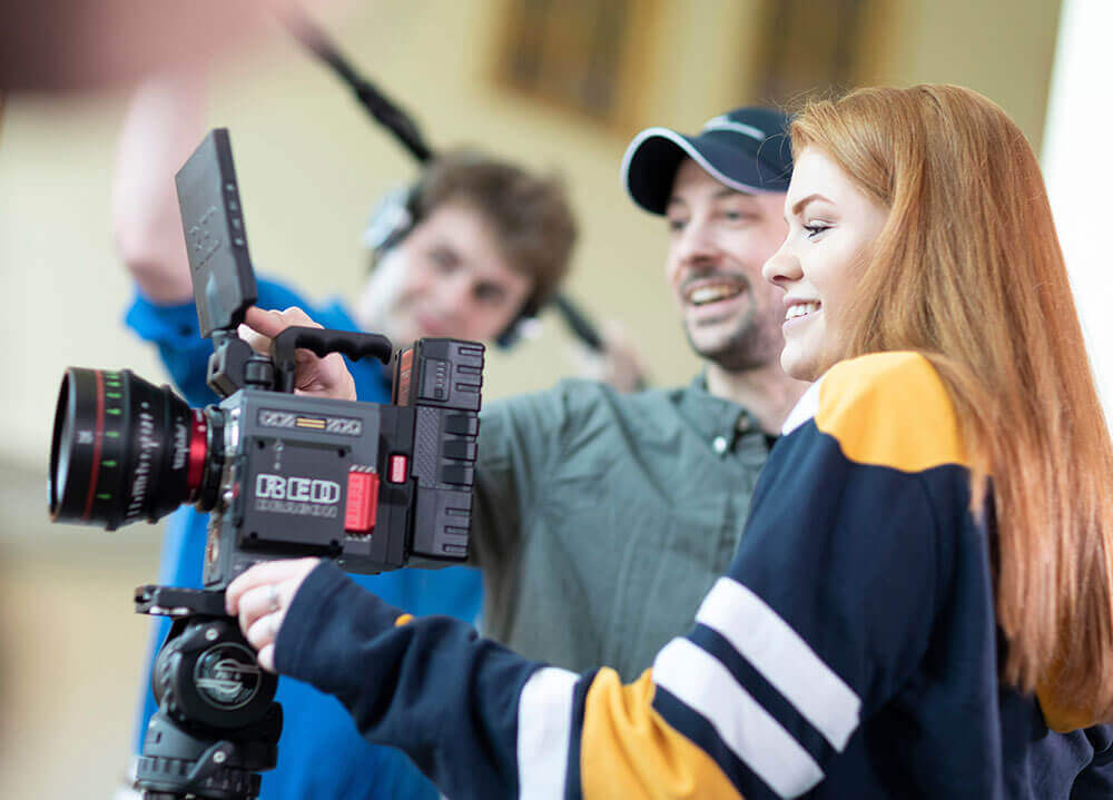 A communications staff member assists two students in holding a cinematic film camera and a boom mic