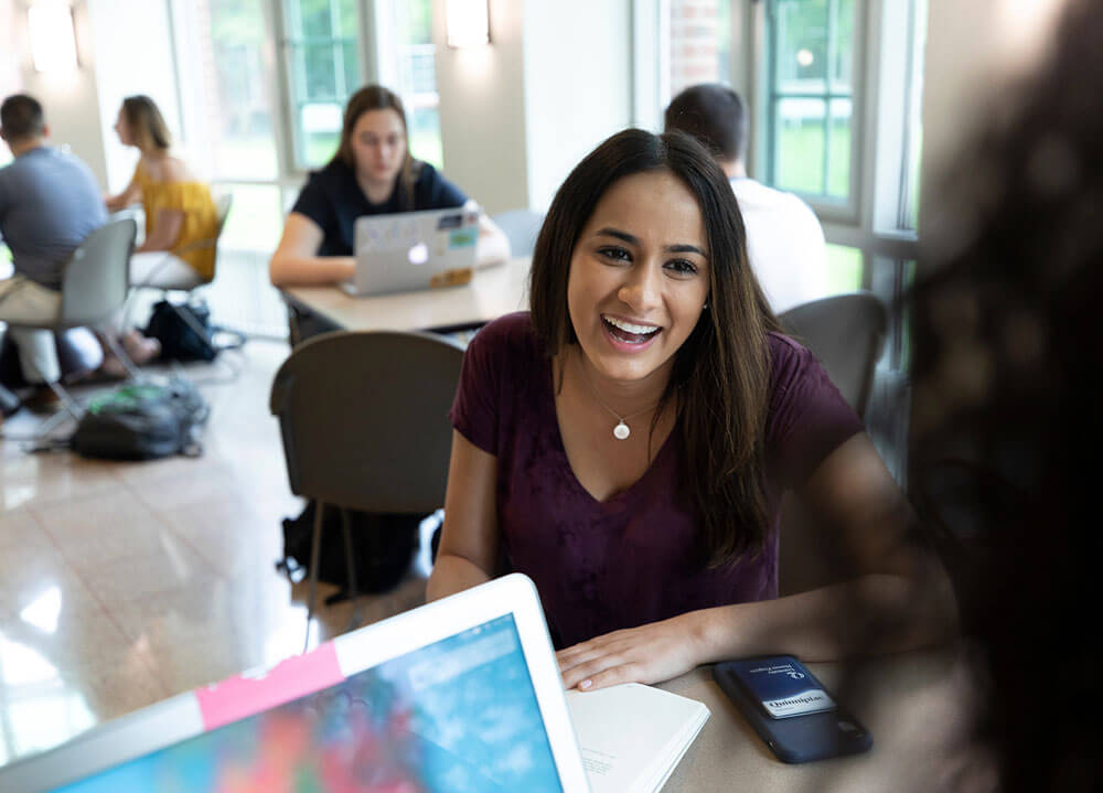 A student smiles at her classmate while they work in an open area in the School of Communications