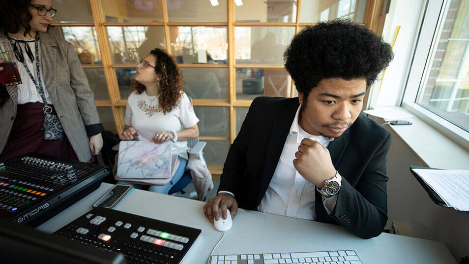 A communications student works on his laptop while editing a podcast episode inside the studio