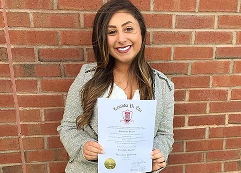 A public relations student poses outside holding a certificate from an honor society