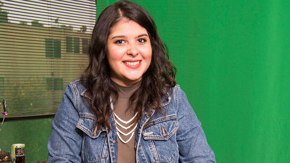 Kayla DeStephen sitting in a director's chair in front of a green screen