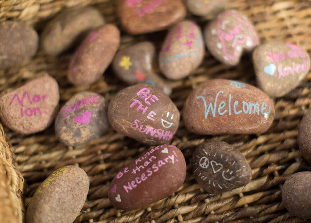 Close-up shot of tiny rocks painted with messages of positivity like "Be happy" and "Welcome"