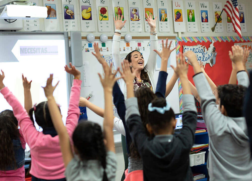 Education alumna Erin Westerman reaches her hands to the sky along with her class full of excited third graders