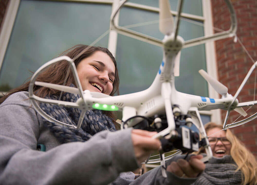 A journalism student smiles as she holds a drone about to take off as part of a course on new technologies in journalism