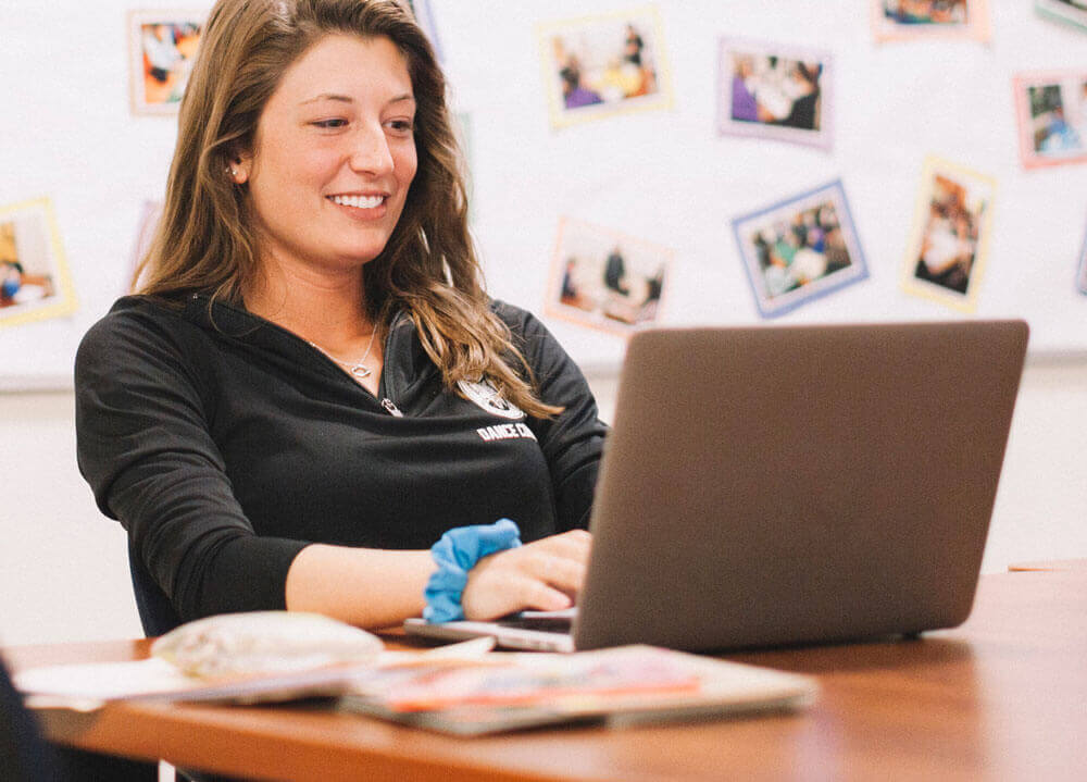 An education student studies at her computer with colorful photos behind her