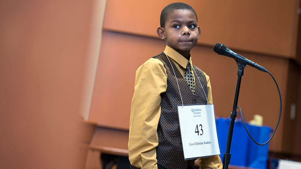 A fourth-grader stands at the microphone and competes in the spelling bee