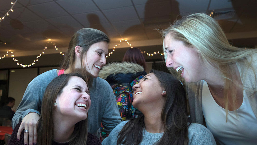 Four school of education students laugh with one another at a Christmas dinner