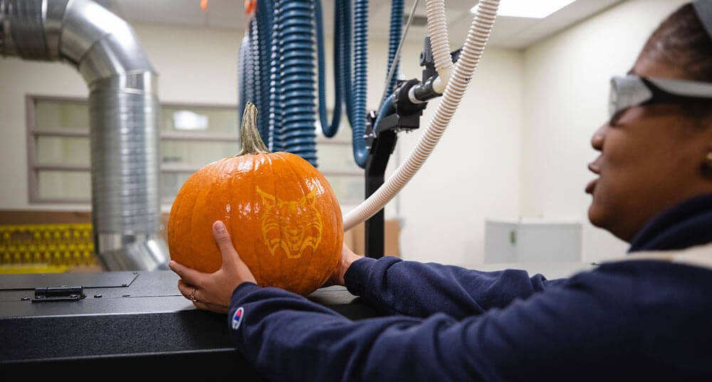 An engineering student places her pumpkin on top of the laser cutter machine