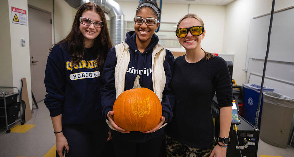 Three engineering students pose with their carved pumpkin